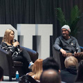 three people sit on stage, two women and one man, one woman is speaking