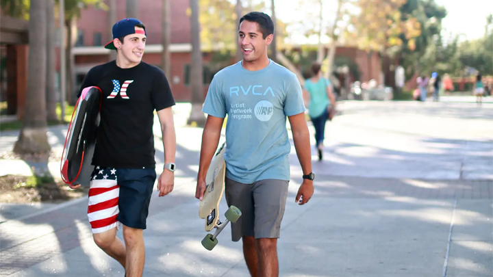 two male students carry skateboards on SDSU campus